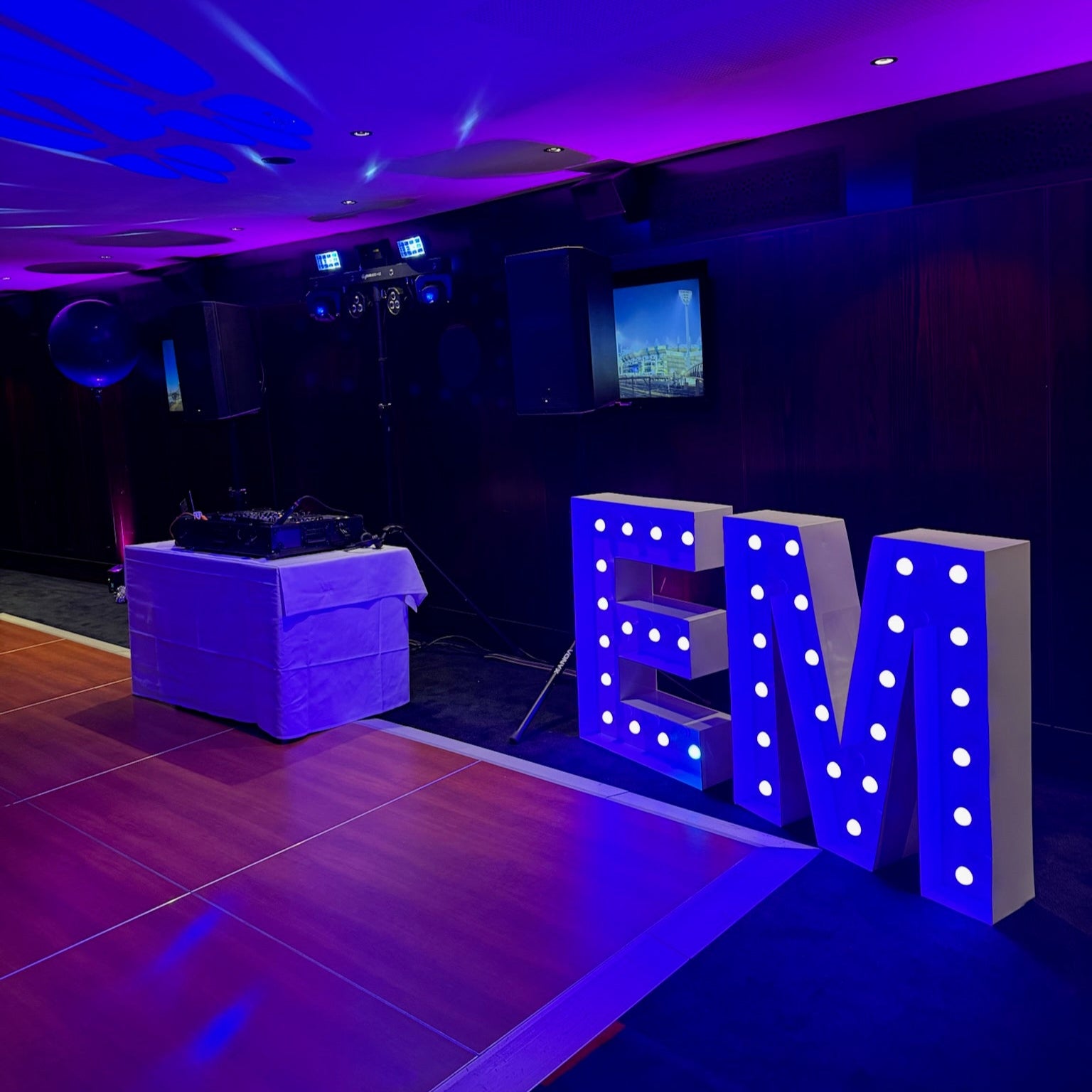 DJ setup with illuminated 1m letters 'EM' with purple coloured globes.