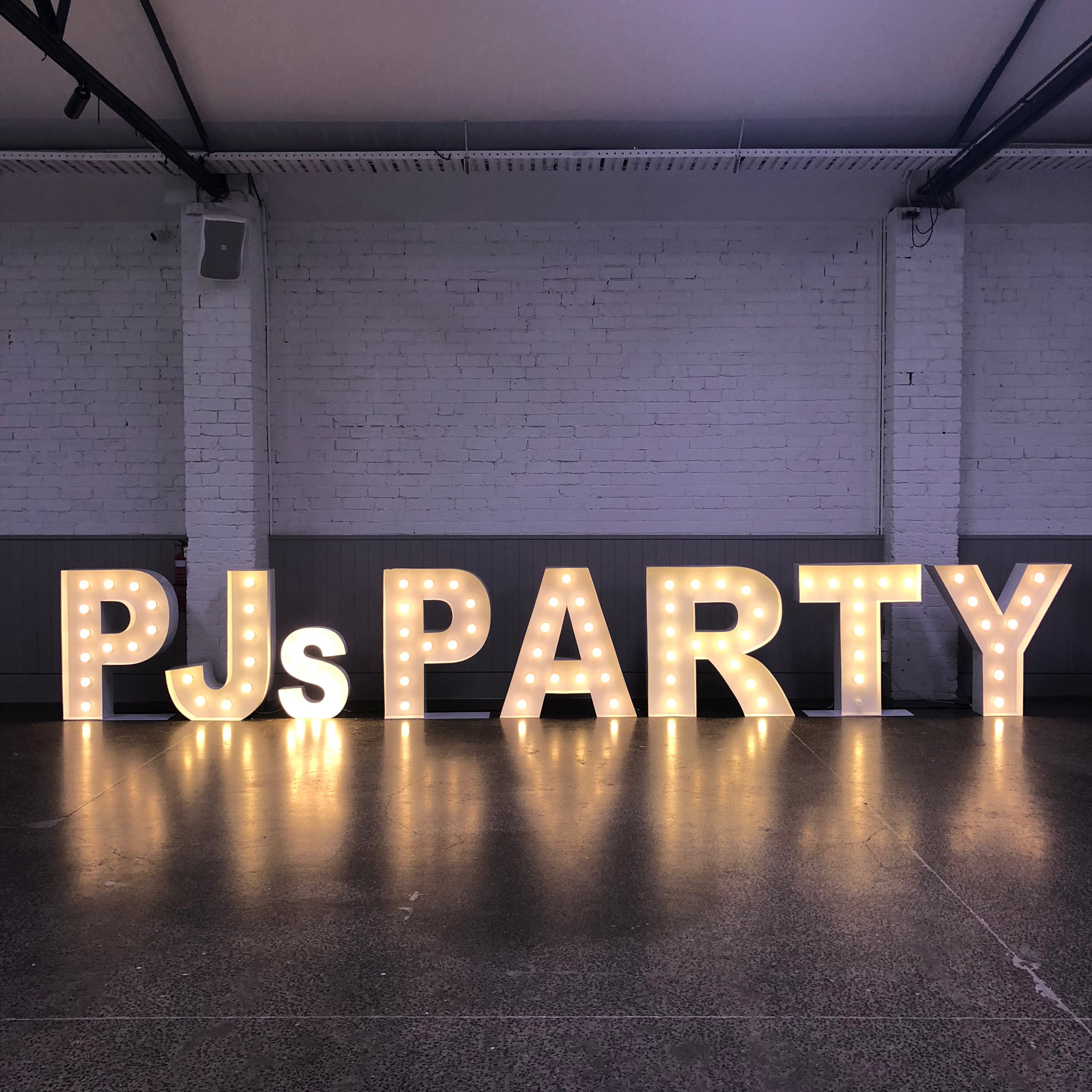 Decorative light-up letters spelling 'PJs PARTY' in a warehouse setting.