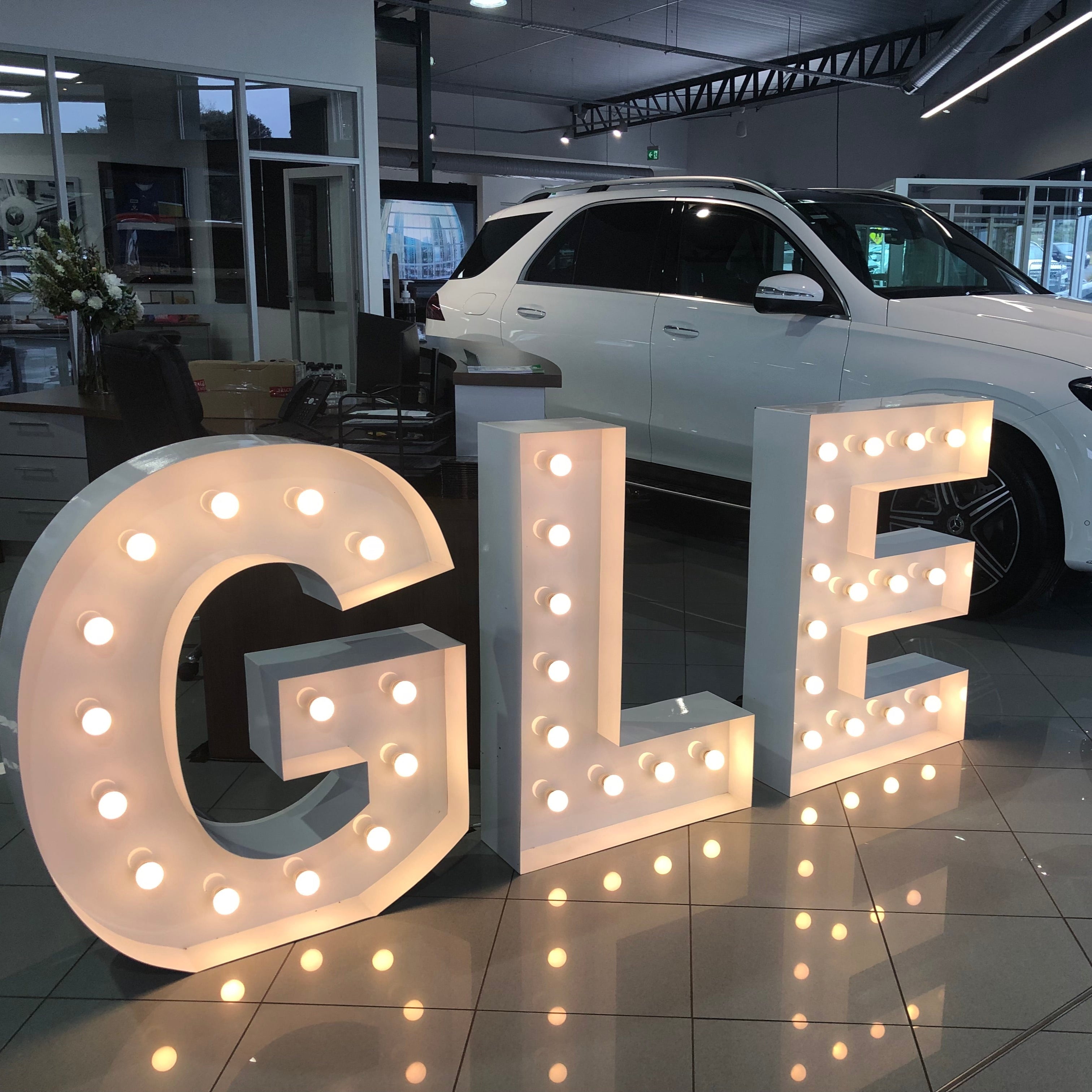 White SUV in a showroom with 1m 'GLE' illuminated letters in the foreground