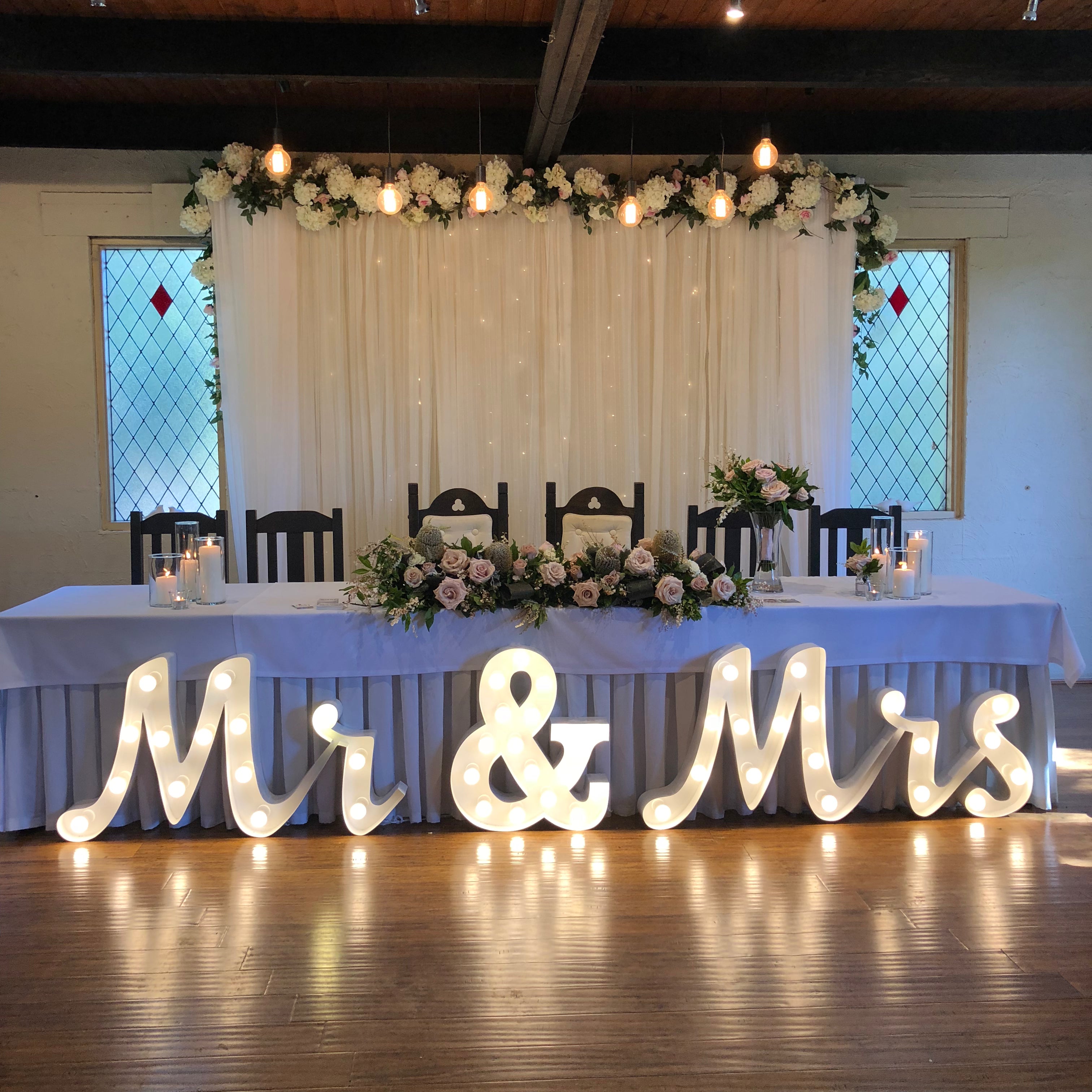 Decorated wedding reception table with floral arrangements, candles, and 'Mr & Mrs' sign.