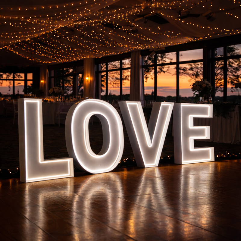 Large illuminated neon letters spelling 'LOVE' in a festive indoor setting with string lights and a sunset view.