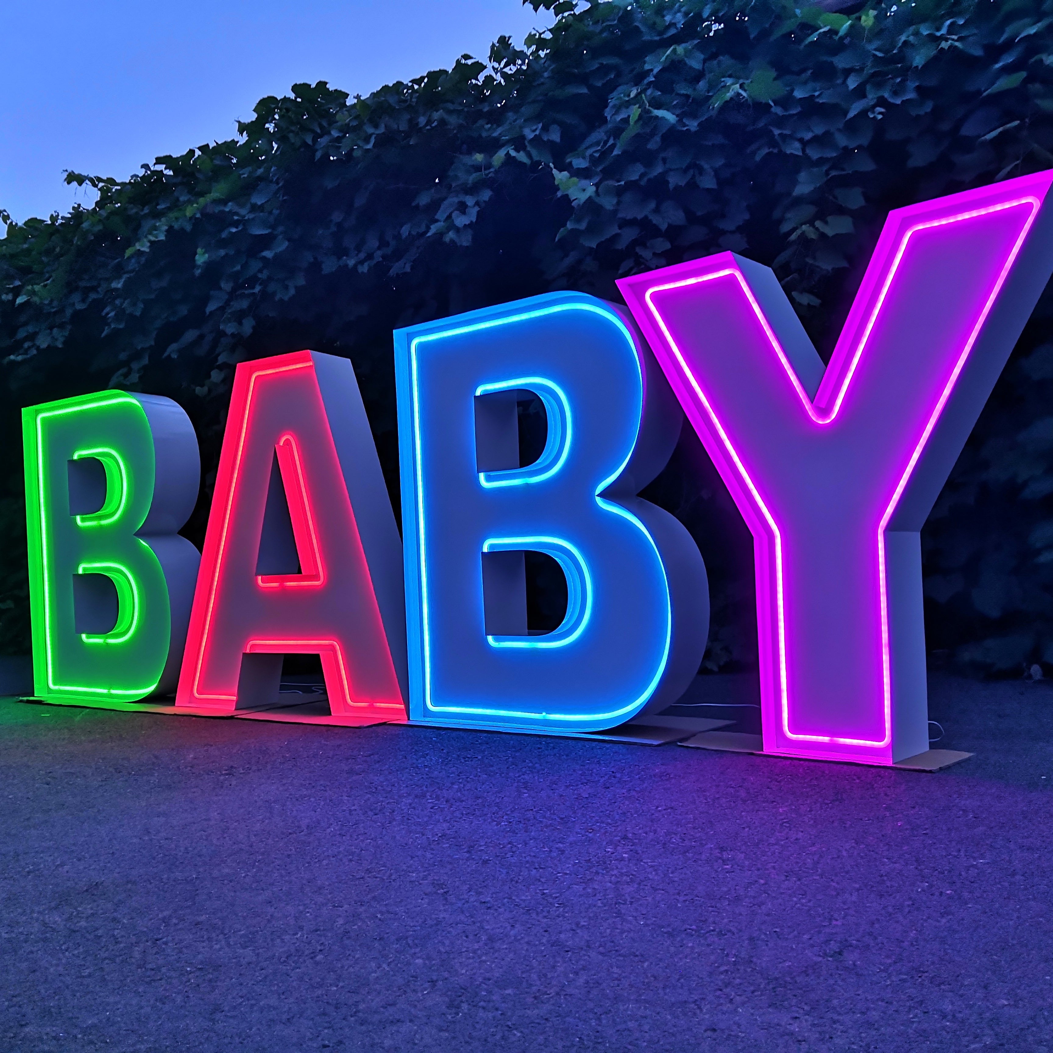 Neon light up letters spelling 'BABY' in colourful lights against a dark background