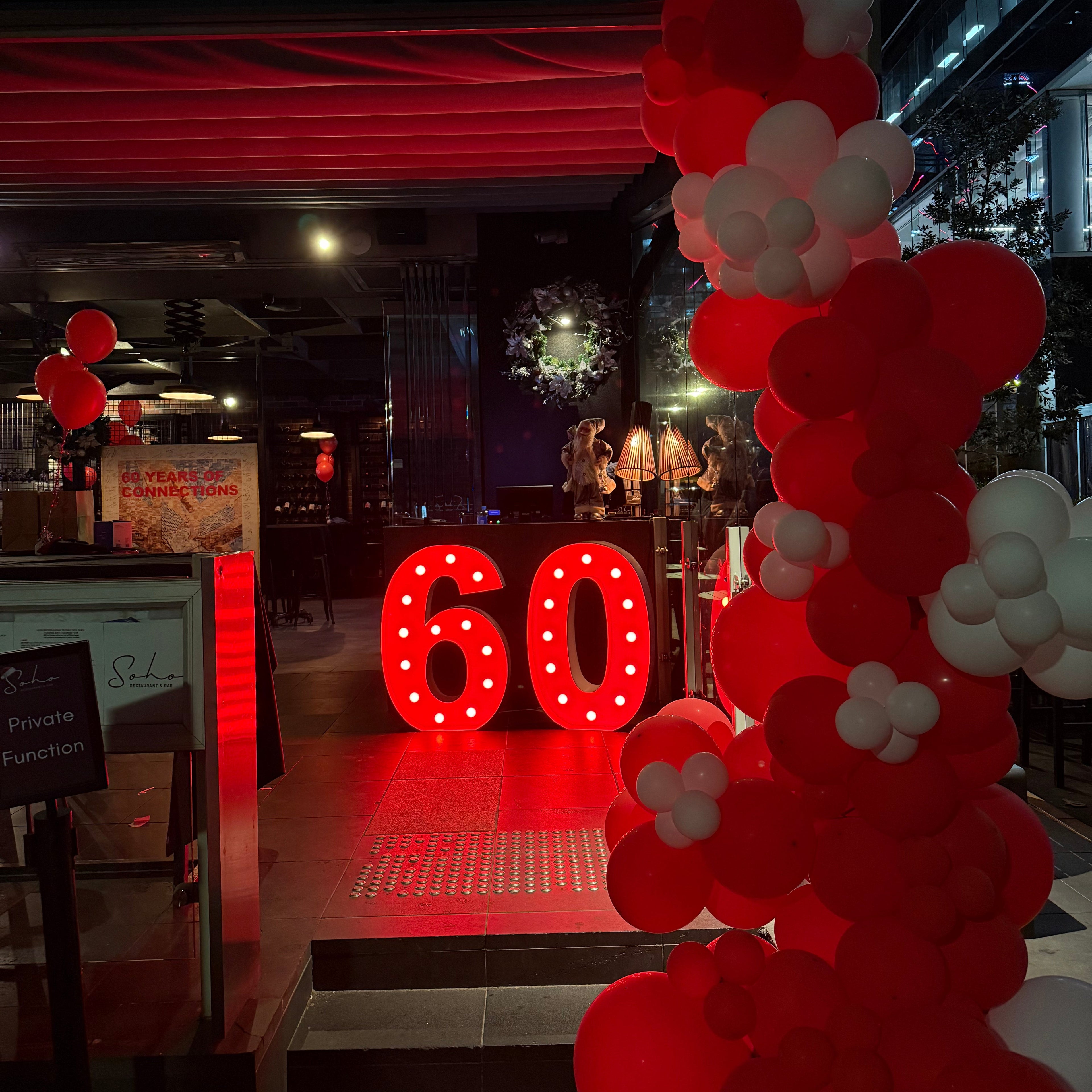 Red globes light up numbers 60 with red and white balloon arch